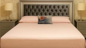 A bedroom with a tufted headboard, a bed with a pink bedspread, a pillow with 'London' text, and two bedside lamps. - Comfort and peace of mind (Santo Domingo Este)