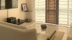 A modern bedroom with a bed, a TV mounted on the wall, a ceiling fan, and a large window with patterned curtains. - Comfort and peace of mind (Santo Domingo Este)