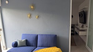 Um sofá azul com uma manta amarela, uma almofada pequena e arte decorativa na parede.