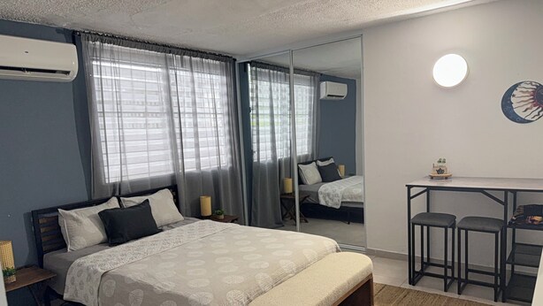 Quarto com cama, mesas de cabeceira, escrivaninha e duas cadeiras, espelho e ar condicionado.