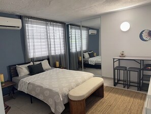 Une chambre à coucher comprenant un lit, des tables de chevet, un bureau avec deux chaises, un miroir et un appareil de climatisation.