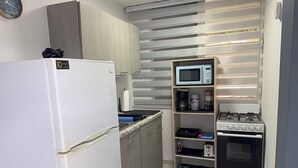 Cozinha compacta com geladeira, micro-ondas, fogão e prateleiras com utensílios de cozinha.