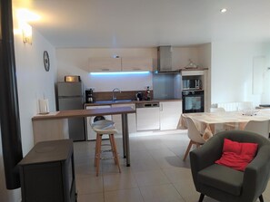 A compact kitchen with modern appliances, a dining area with a table and chairs, and a small stool. - Gîte Lezinio - LE PONT-DE-MONTVERT (LE PONT-DE-MONTVERT)