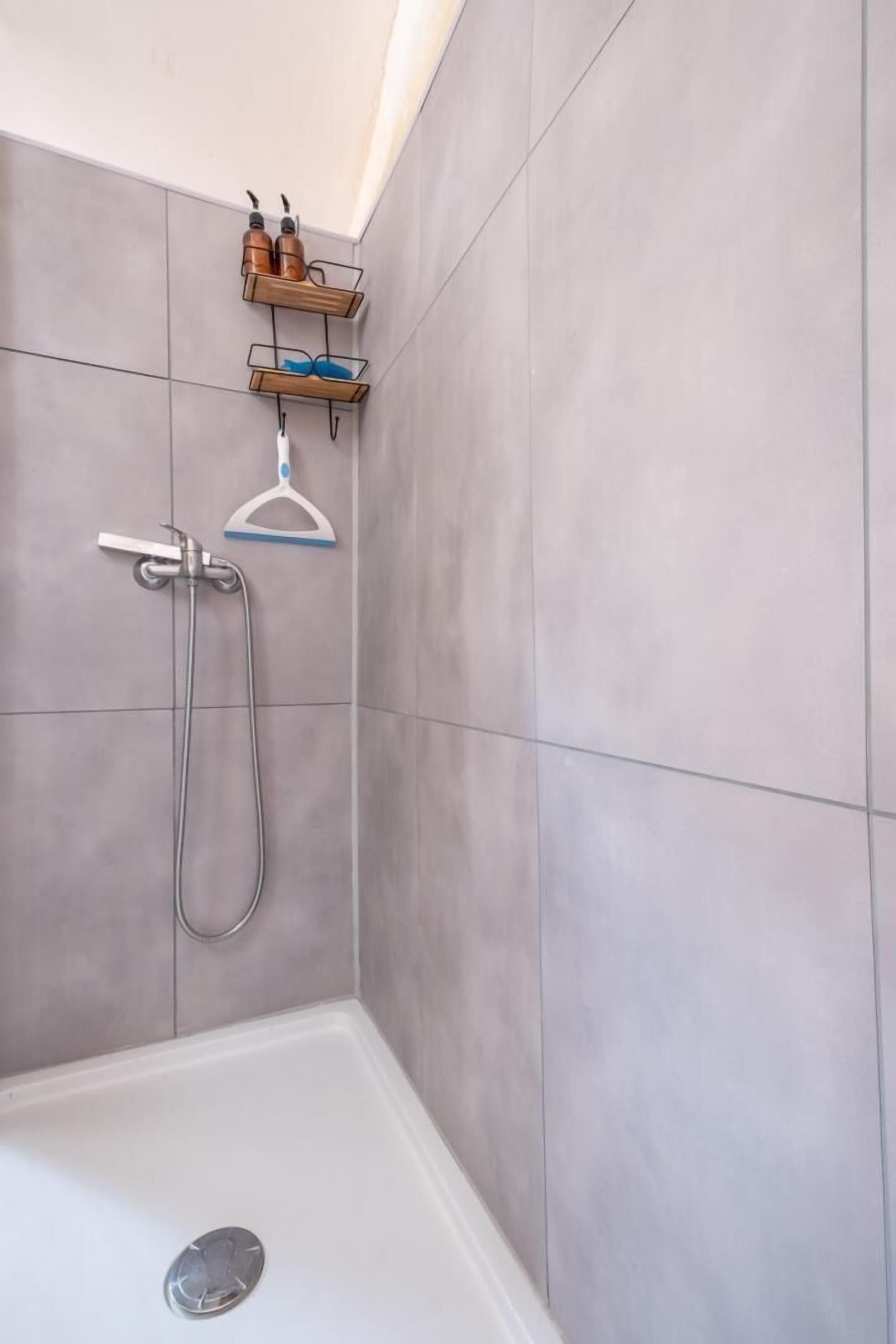 A shower with a handheld showerhead and a wall-mounted faucet.