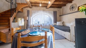 A cozy room with a wooden staircase, a dining table set with plates and glasses, a bed with pillows, and a clock on the wall. - Gîte de l'Escoutal 2/4 persons (LE BLEYMARD)