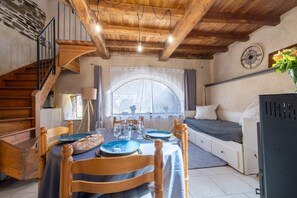 A cozy room with a wooden staircase, a dining table set with plates and glasses, a bed with pillows, and a clock on the wall. - Gîte de l'Escoutal 2/4 persons (LE BLEYMARD)