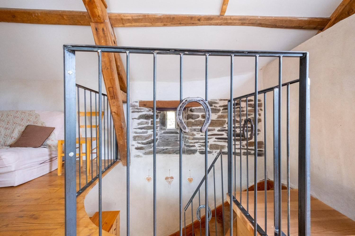 A loft bedroom with a stone wall, a wooden staircase, and a metal gate.
