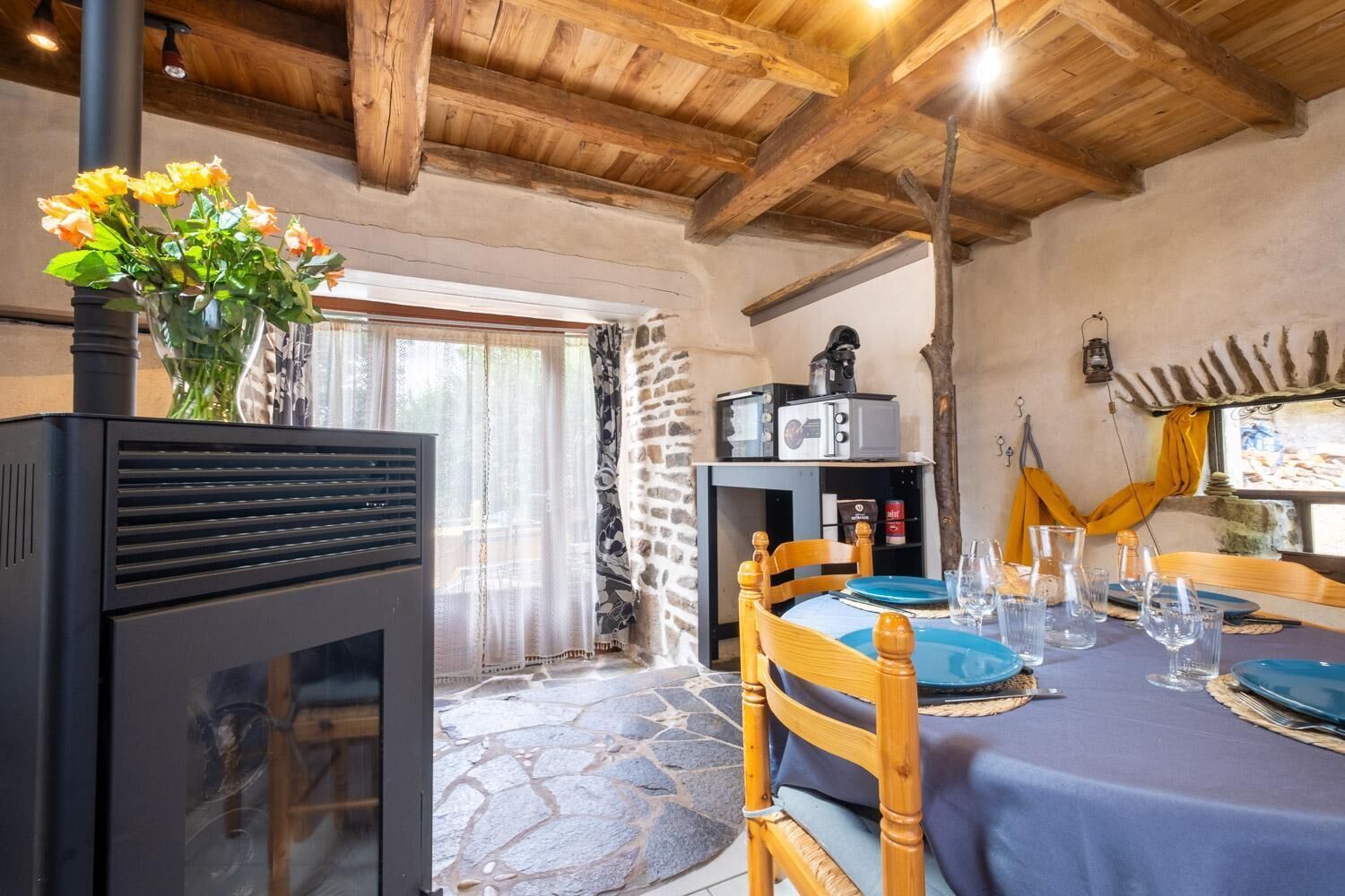 A rustic dining area with a stone floor, wooden furniture, and a fireplace.