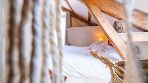 A cozy attic bedroom with a sloped ceiling, a bed with white linens, and a lamp on the nightstand. - Gîte de l'Escoutal 2/4 persons (LE BLEYMARD)