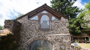 A stone building with a large arched window, a small balcony, and a metal gate. - Gîte de l'Escoutal 2/4 persons (LE BLEYMARD)
