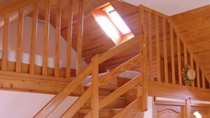 En trätrappa med ett takfönster som leder upp till ett rum med en dörr och en väggmonterad lampa.