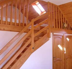 Eine Holztreppe mit Oberlicht, die zu einem Raum mit einer Tür und einer Wandleuchte führt.