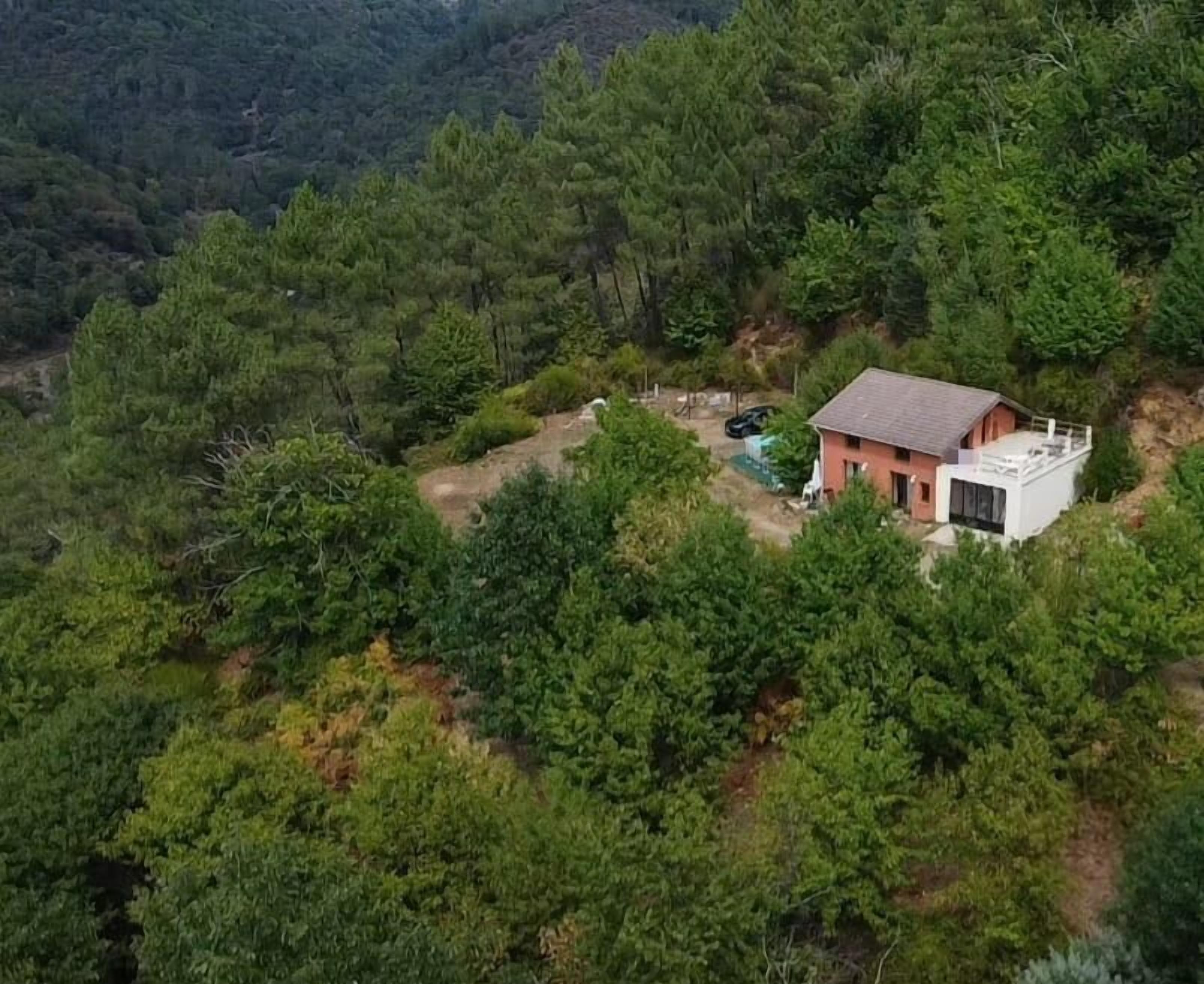 A house surrounded by dense forest, with a visible patio area and a satellite dish.