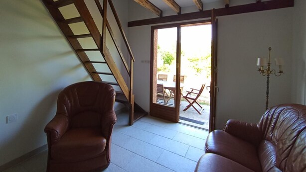 Une pièce avec un escalier, deux fauteuils en cuir, un lustre et une porte-fenêtre coulissante donnant sur l’extérieur.