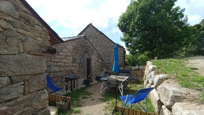 Un edificio de piedra con un pequeño patio, una mesa con sillas y una sombrilla azul.