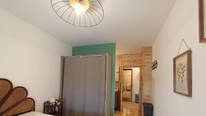 Un dormitorio con cama, piso de madera, ventilador de techo, puerta que da a otra habitación y un cuadro enmarcado en la pared.