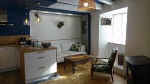 Un espacio habitable compacto con kitchenette, un sofá, una mesa de centro de madera, una silla y una decoración de cabeza de toro en la pared.