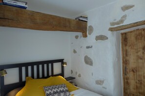 Une chambre à coucher avec une tête de lit en bois, un lit avec une literie jaune, une table de chevet avec une lampe et un mur en pierre.