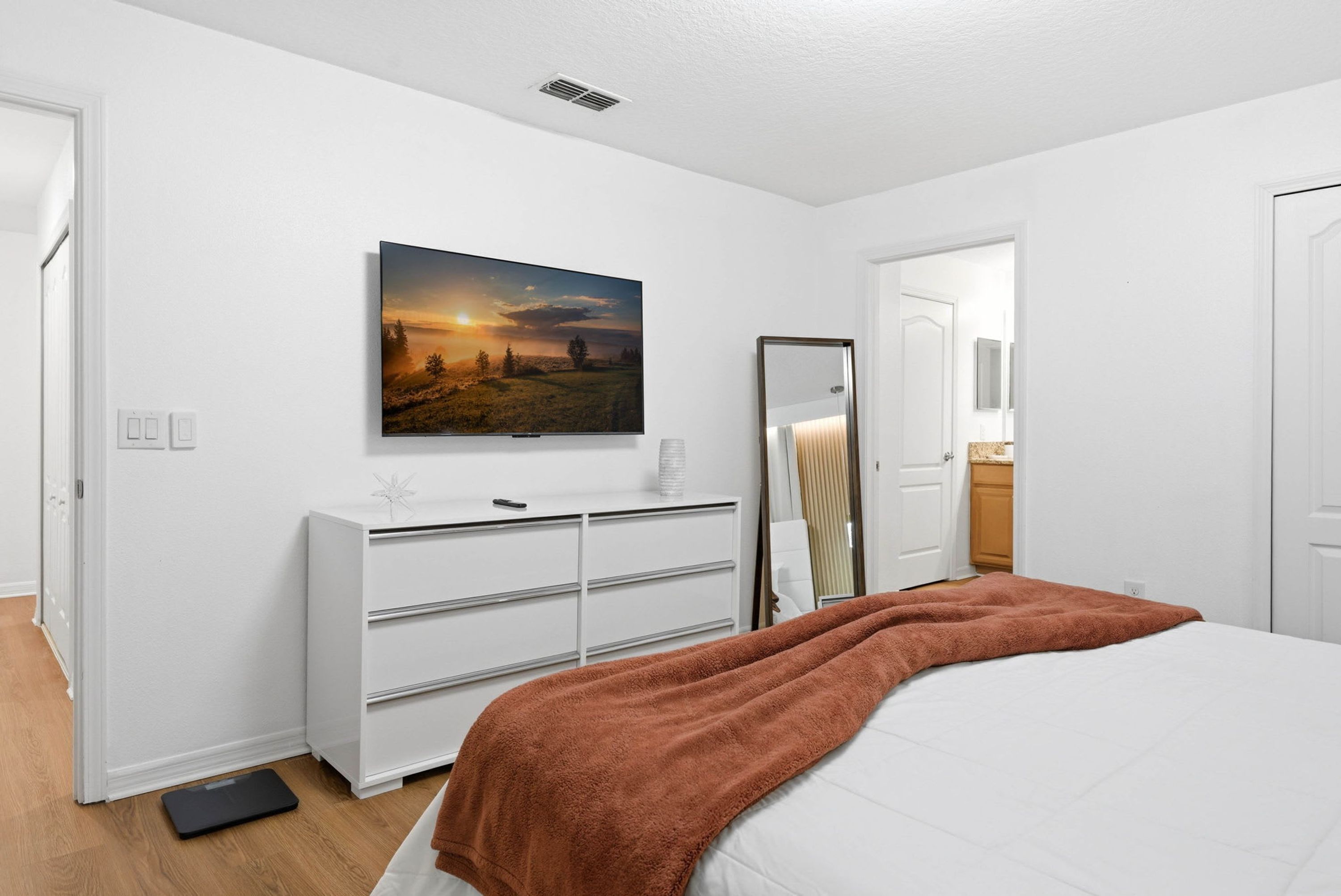 A bedroom with a bed, a dresser, a mirror, and a painting on the wall.