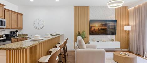 Una cocina moderna con una isla central, un área de comedor con taburetes de bar, un sofá y una mesa de centro redonda.