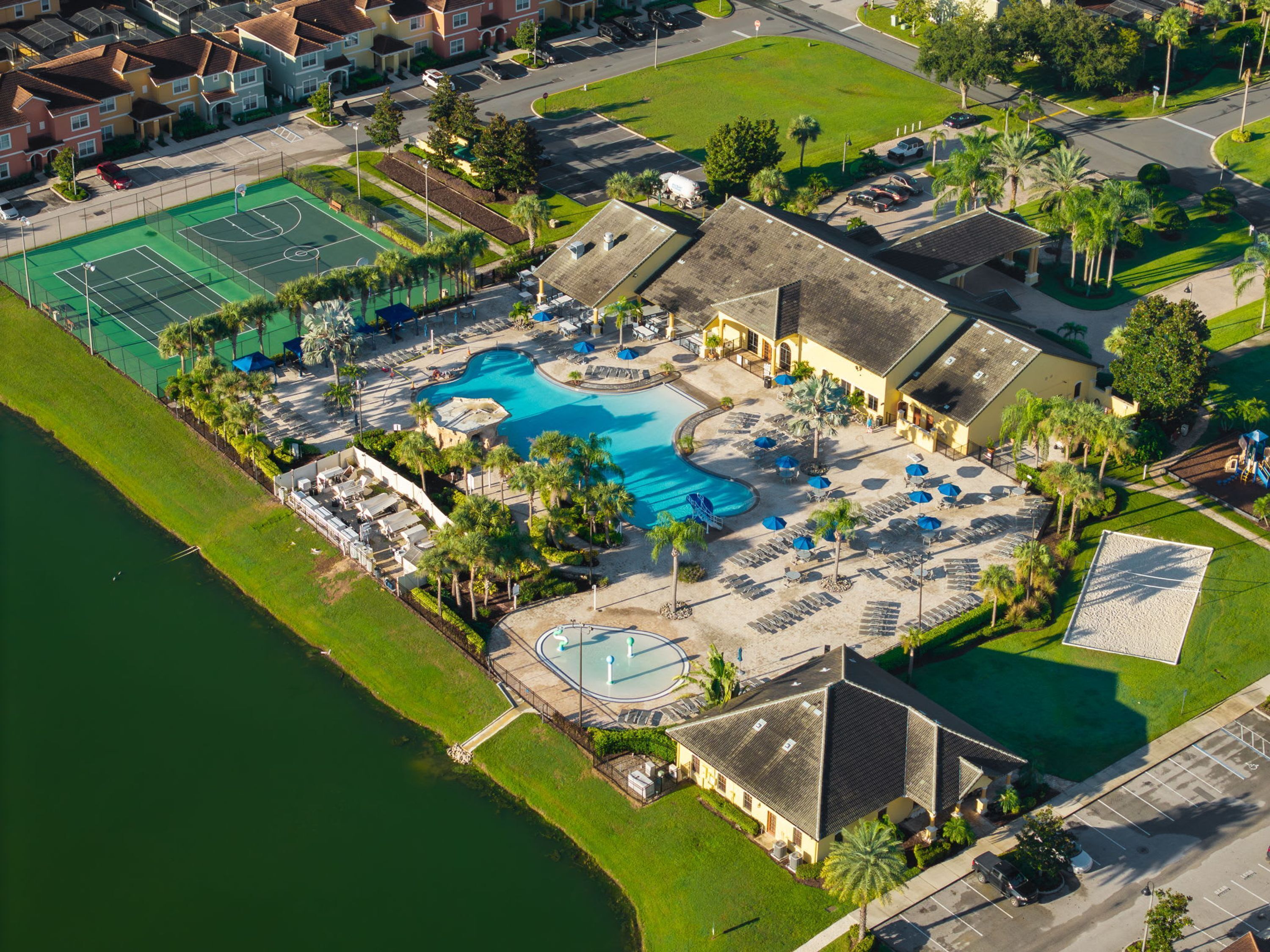An aerial view of a resort with a swimming pool, tennis courts, and a beach area.