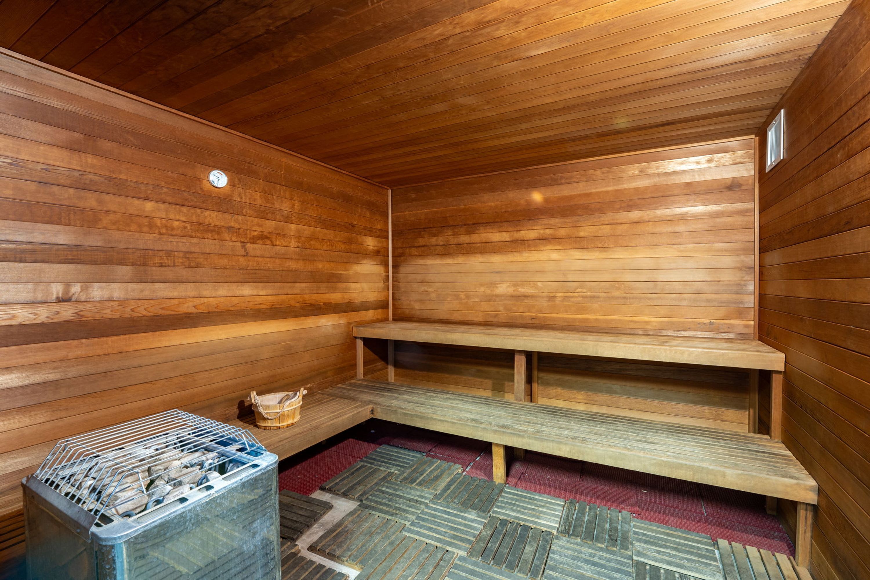 A sauna with wooden walls, benches, and a metal container.