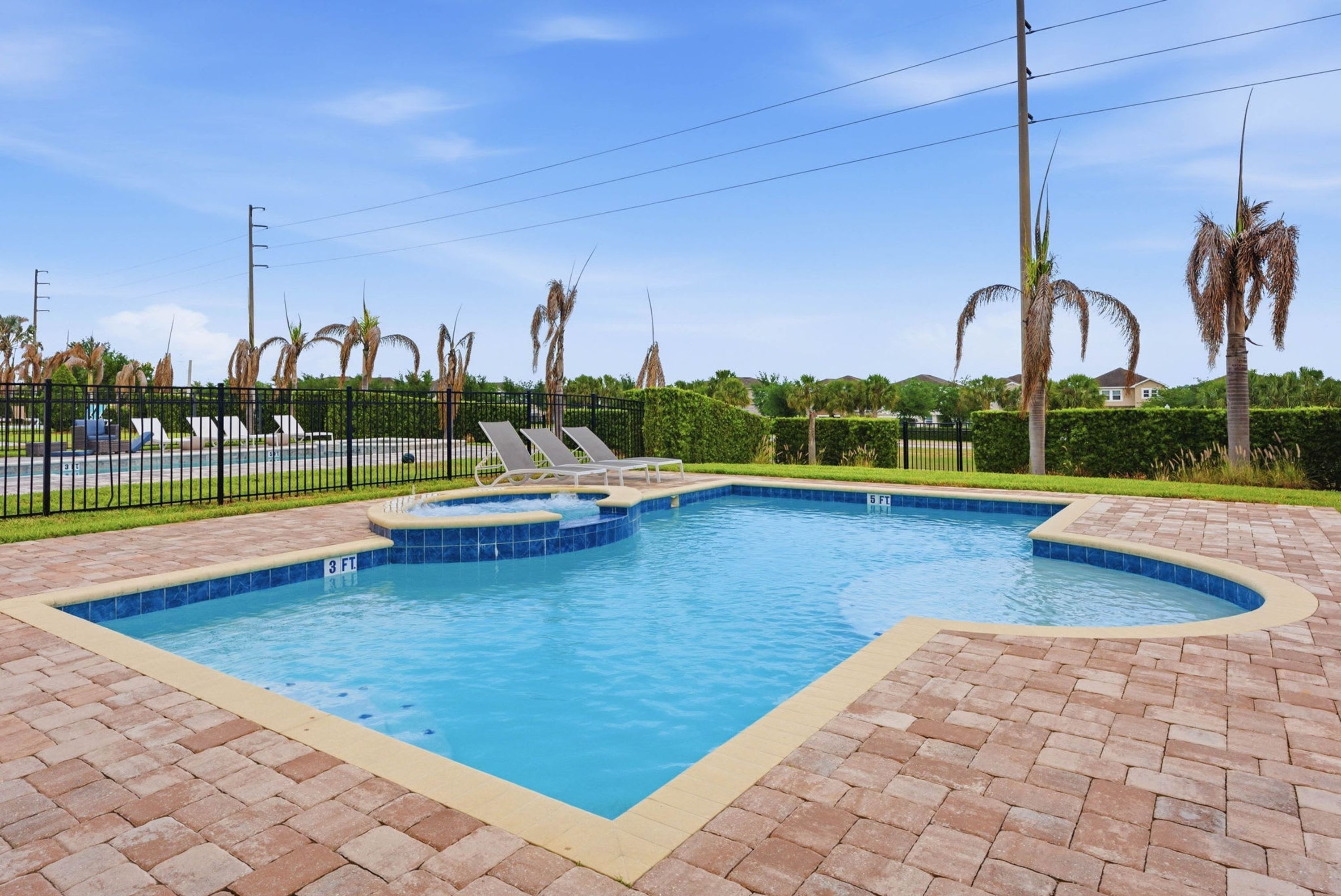 Une piscine rectangulaire dont le bord est recouvert de carreaux, entourée d’une terrasse en briques.