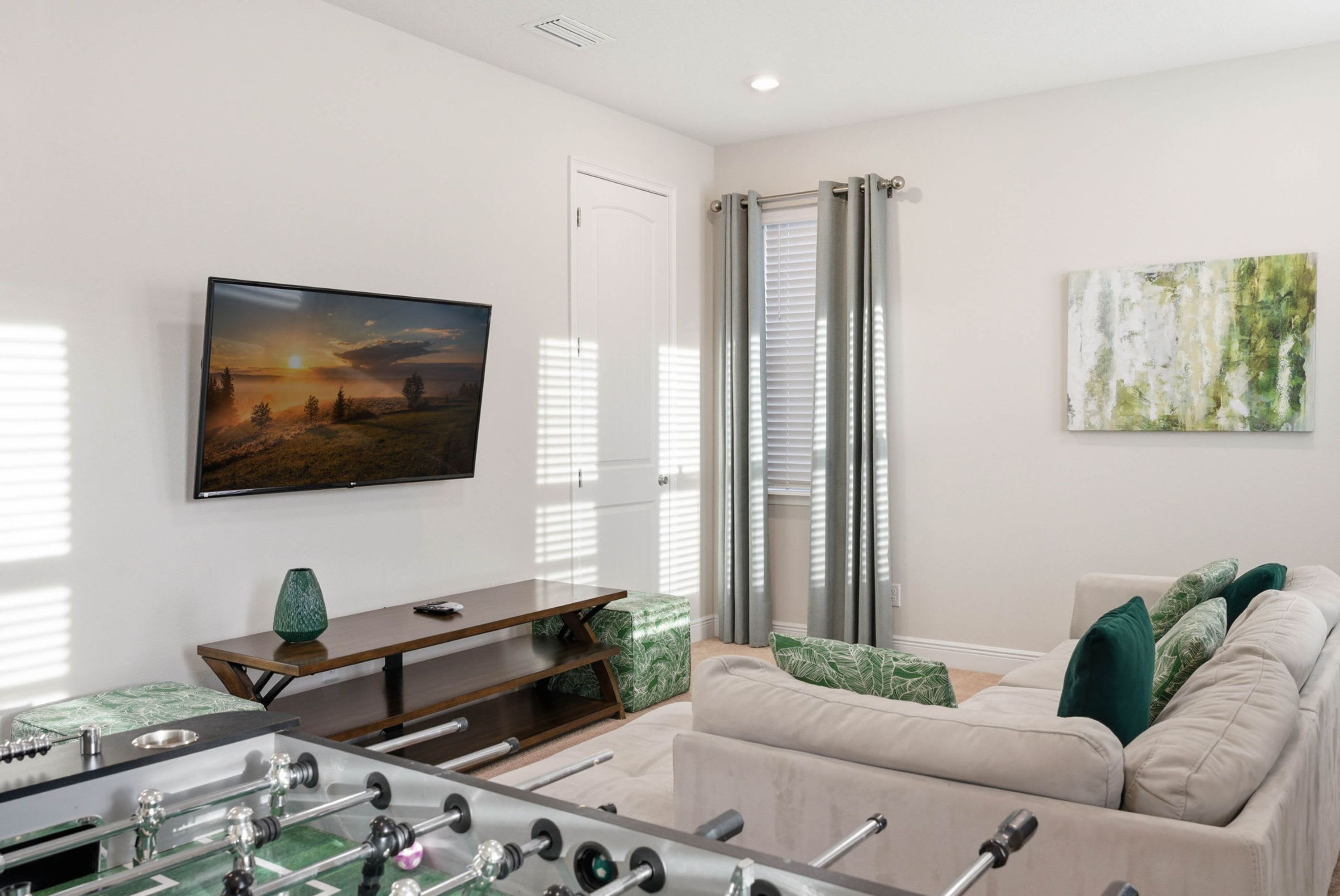 A living room with a foosball table, a flat-screen TV, a sofa, and a painting on the wall.
