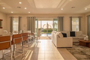 A spacious living area with a dining table, chairs, a sofa, and a view of a swimming pool. - 4BR Getaway Spacious Beautiful Great Location (Kissimmee)