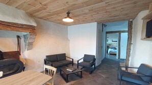 A cozy living room with a fireplace, a dining area, and a view into another room. - Gîte Lozère Bleue 4/5 persons (LES LAUBIES)