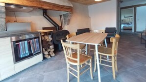 A rustic interior with a wooden table and chairs, a stove, and a fireplace. - Gîte Lozère Bleue 4/5 persons (LES LAUBIES)