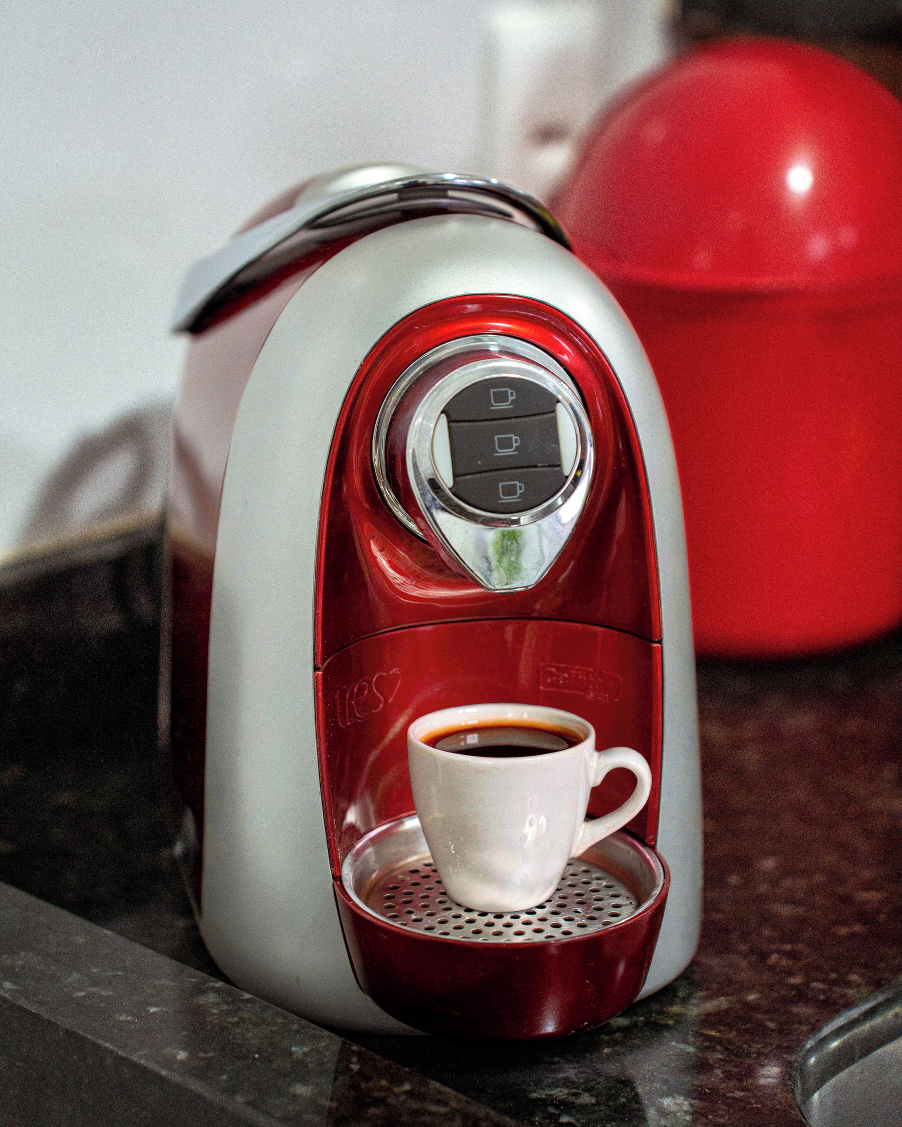 Una cafetera roja y plateada con una taza de café sobre su bandeja de goteo.