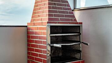 Un horno de ladrillo al aire libre con una chimenea metálica, una mesa con una computadora portátil y vistas al cielo a través de una ventana.