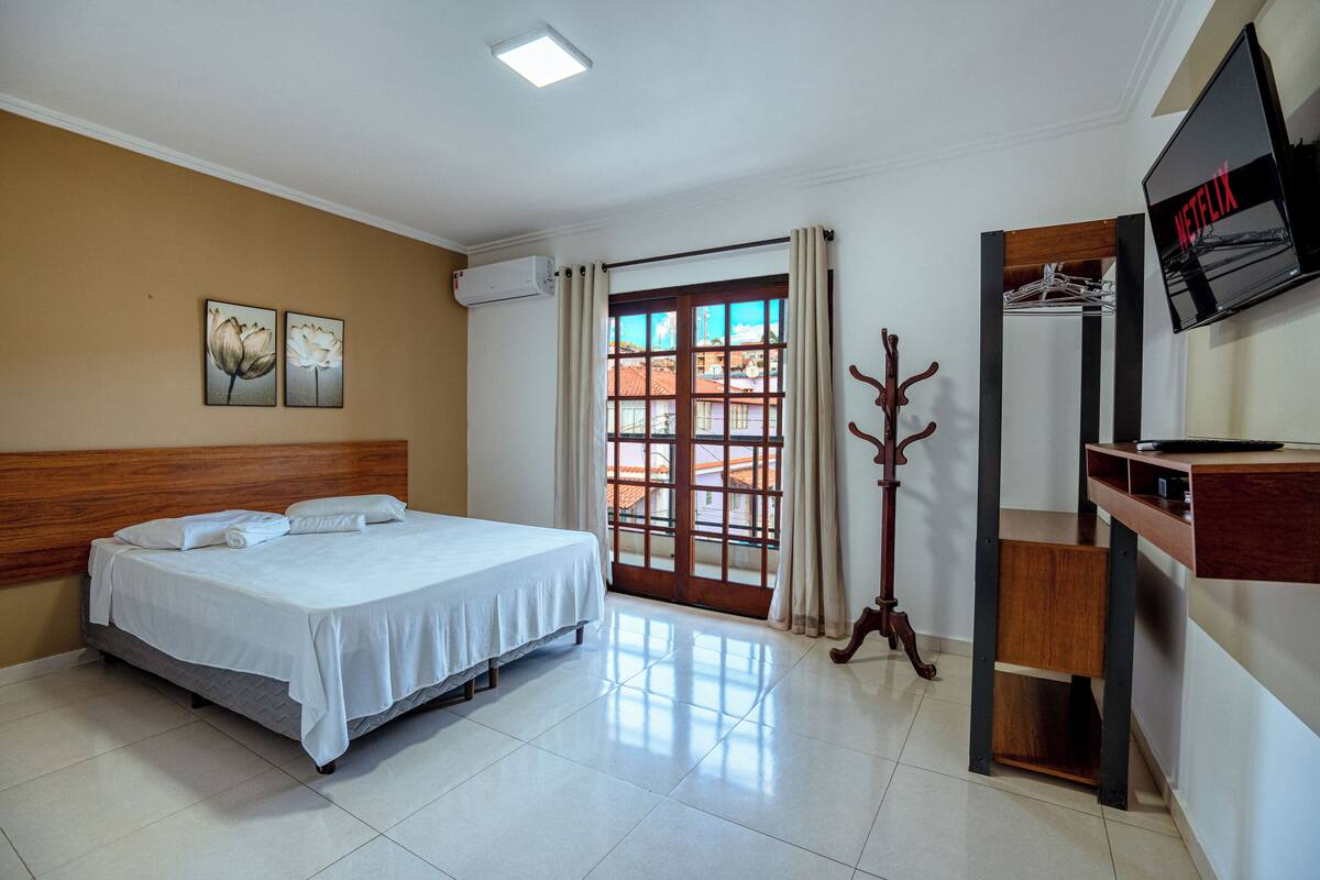 Une chambre d’hôtel avec un lit, une télévision, un porte-manteau et une fenêtre avec des rideaux.