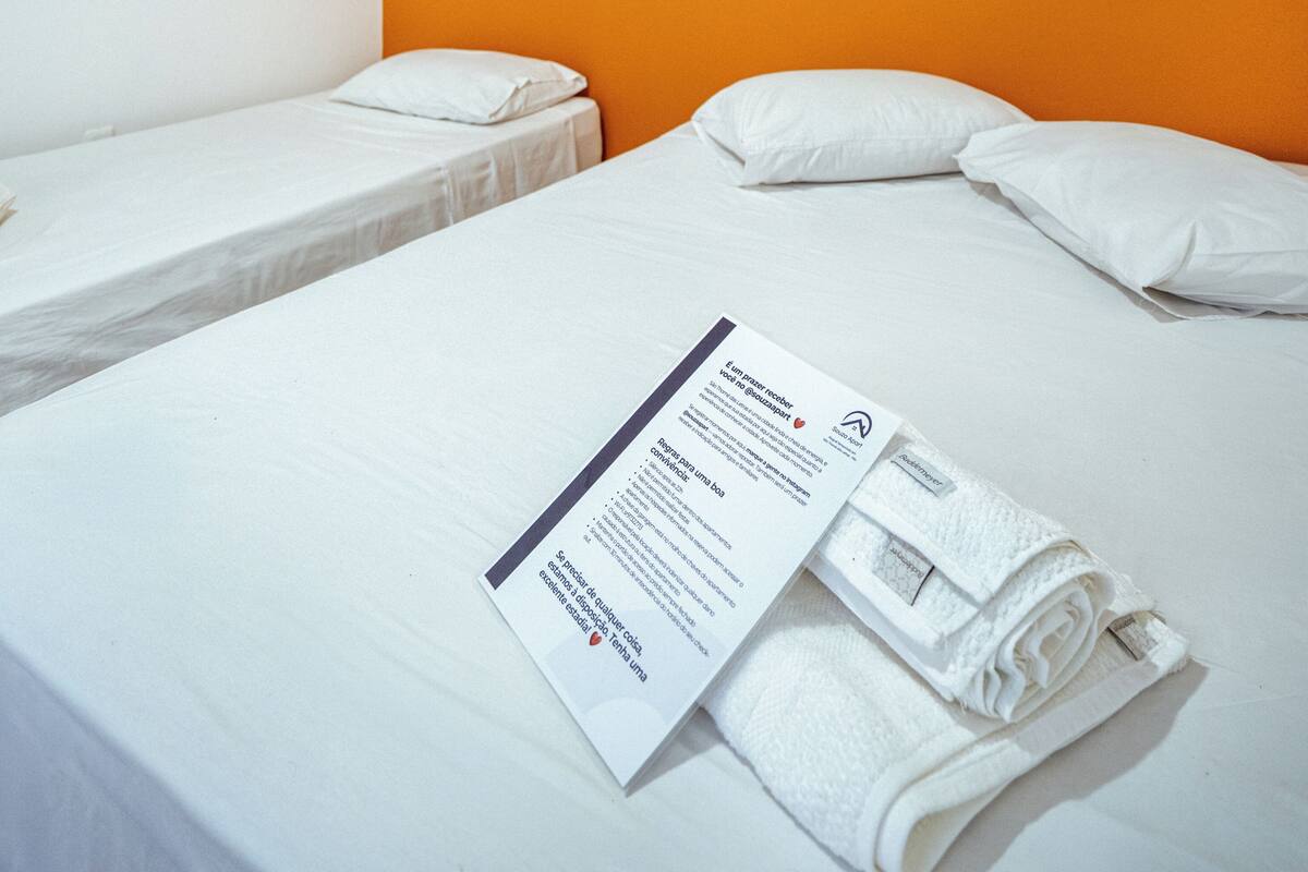 Une chambre d’hôtel avec deux lits simples, du linge de lit blanc, un mur d’accent orange et deux tableaux encadrés.