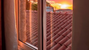 A window with a view of a red-tiled roof and a sunset. - Souza Apart 2 - Apartamentos completos (Sao Thome das Letras)