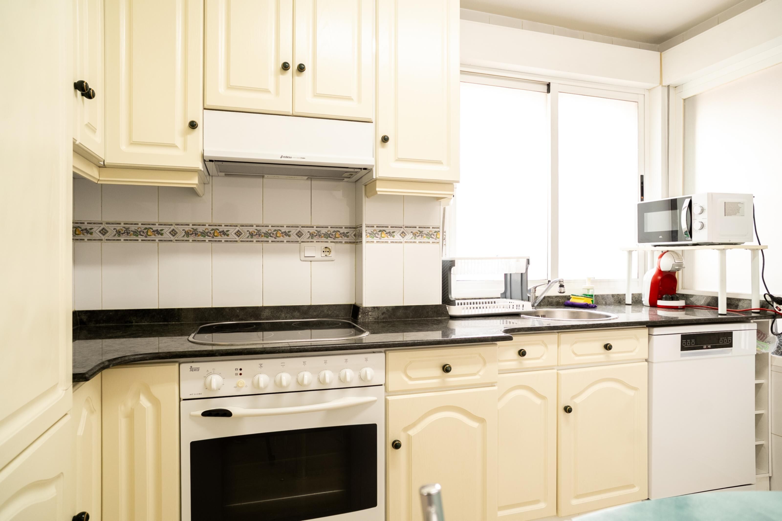 A kitchen with white cabinets, a stove, a microwave, and a dishwasher.