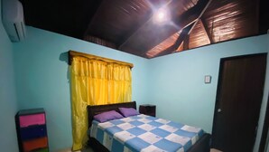 A bedroom with a bed, a nightstand, a colorful storage unit, and a door. - Marisol House (Quepos)