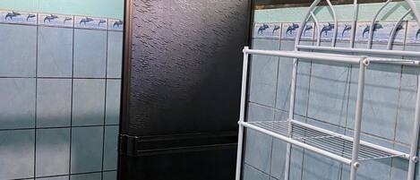 A bathroom with a tiled wall, a black door, a white shelf, and a blue trash bin.