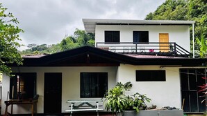 A two-story house with a balcony, a dining area with a bench, and potted plants. - Marisol House (Quepos)