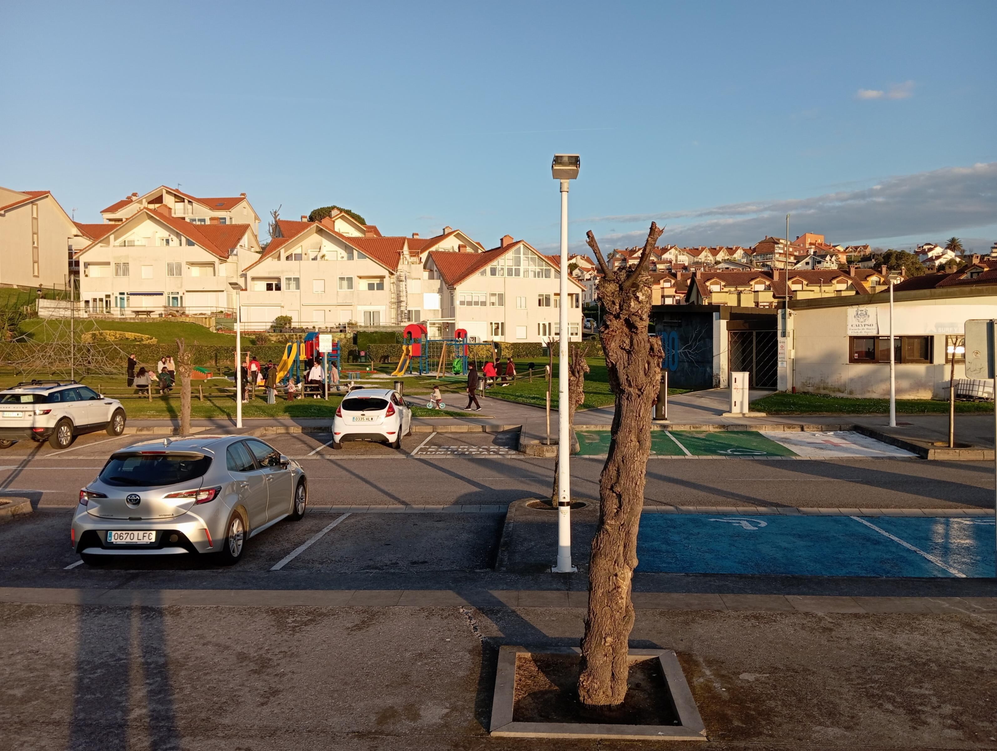 Zona residencial con casas, un parque infantil y un estacionamiento con automóviles.