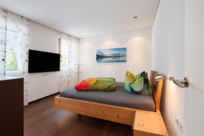 A modern bedroom with a bed, a TV, and a painting of a mountain landscape. - Villa in Tyrol With Pool (Stanz bei Landeck)