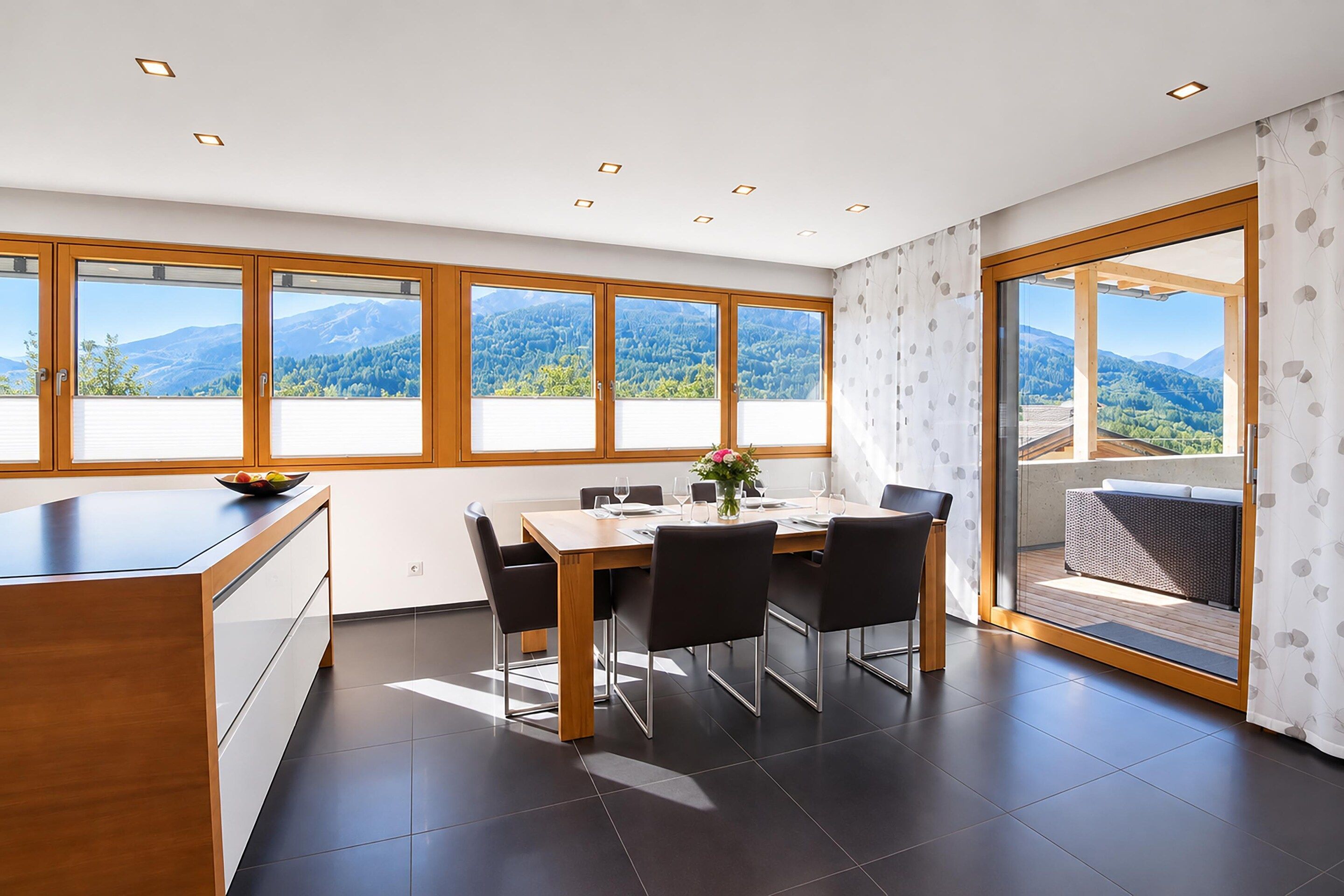 Ein moderner Essbereich mit großem Tisch, Stühlen und Bergblick durch große Fenster.