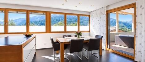 Ein moderner Essbereich mit großem Tisch, Stühlen und Bergblick durch große Fenster.