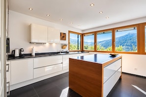 A modern kitchen with a central island, white cabinetry, and a large window offering a mountain view. - Villa in Tyrol With Pool (Stanz bei Landeck)