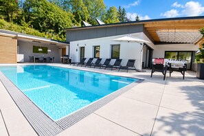 A modern outdoor swimming pool area with lounge chairs, a barbecue grill, and a covered seating area.