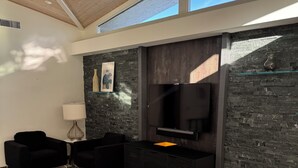 Uma sala de estar moderna com um sofá grande, uma mesa de centro, uma TV de tela plana e uma parede de destaque em pedra.