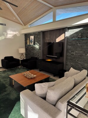 Ein modernes Wohnzimmer mit einer großen Couch, einem Couchtisch, einem Flachbildfernseher und einer Wand mit Steinoptik.
