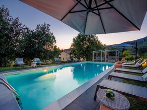 A swimming pool with lounge chairs and umbrellas, surrounded by trees and a hill in the background. - Apartment in Tuscany With Scenic Pool Views (Capannori)