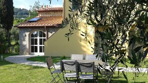 A stone building with a tiled roof, a glass door, and a small patio with a table and chairs. - Apartment in Tuscany With Scenic Pool Views (Capannori)